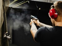 A male facing forward shooting a firearm at a target