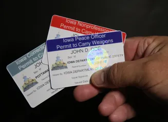 A hand holding 3 weapon permit cards